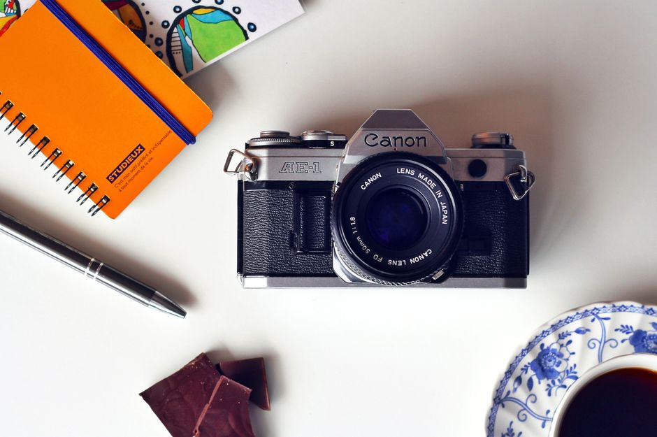 Vintage Canon camera with notepad, pen, and coffee on a desk for a creative workspace vibe.
