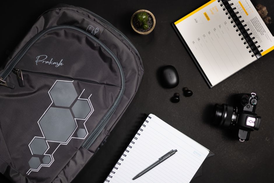 Overhead view of a modern workspace featuring a backpack, camera, and stationery items.